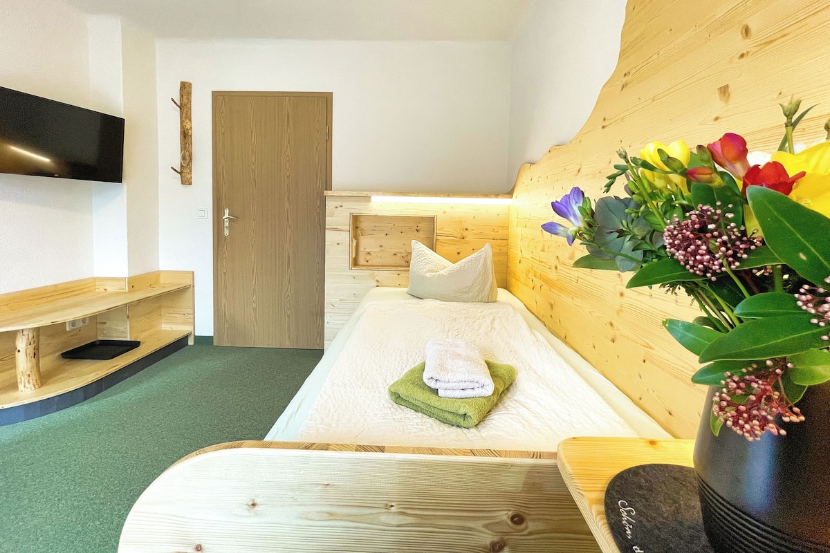 A room with a wooden bed, a flat-screen TV, a wooden bench, and a wall-mounted TV.