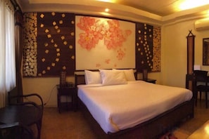 A hotel room with a large bed, a desk, and a chair. There is a wall with a floral design and a large window. - Sri Ping Resort (Chiang Mai)