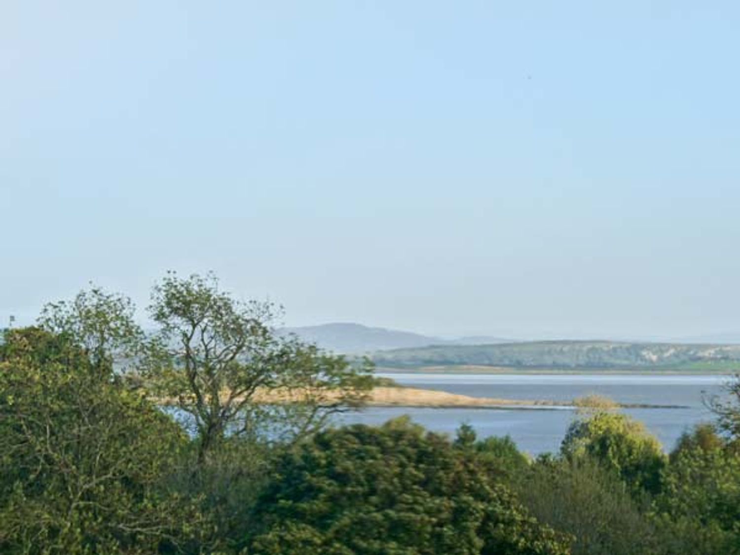 A view of a lake with trees in the foreground and hills in the background.