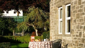 Un patio al aire libre con una mesa preparada para dos, un edificio de piedra y un árbol de fondo.