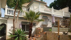 Un immeuble de deux étages avec une façade blanche, un balcon doté de balustrades blanches et un escalier en pierre menant à l’étage supérieur.