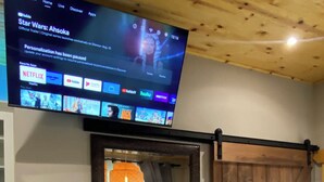 Una habitació amb televisió que mostra 'Star Wars: Ahsoka' a Disney+, una porta corredissa de fusta, una cadira blava i una taula petita amb un globus i llibres.