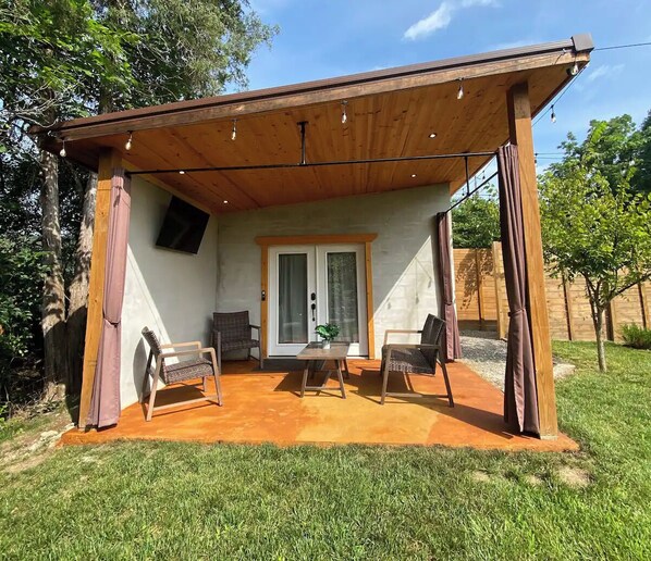 Une terrasse couverte avec deux chaises et une table, une porte-fenêtre coulissante et une pergola en bois au-dessus.