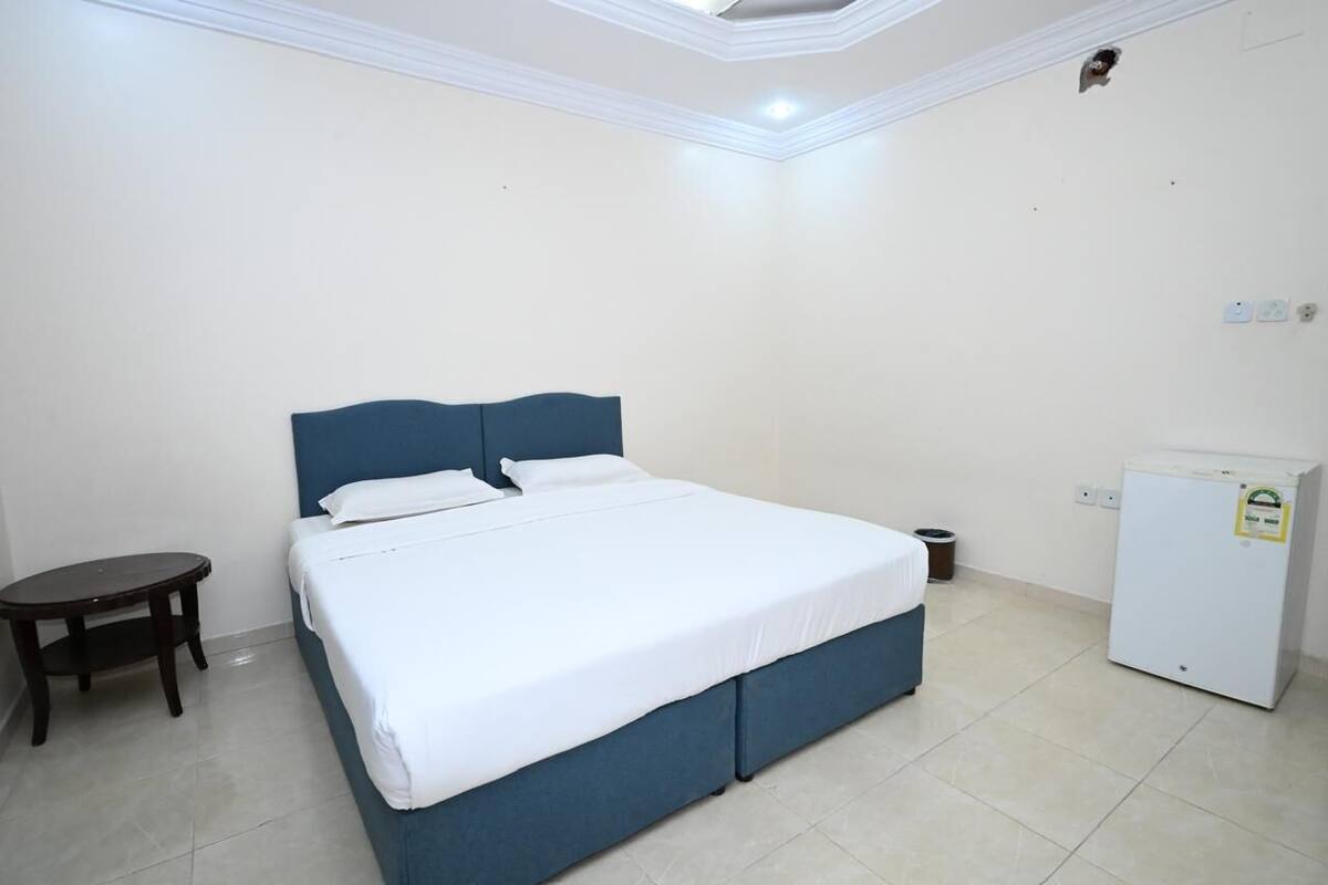 A bedroom with a bed, a small table, and a refrigerator.
