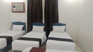 Une chambre d’hôtel avec quatre lits simples, une petite table et un appareil de climatisation fixé au mur.