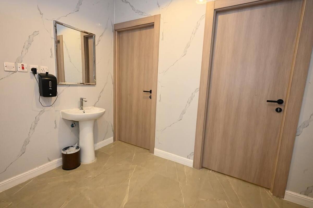 A bathroom with a marble wall, a sink, a mirror, and two wooden doors.
