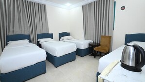 Une chambre d’hôtel avec trois lits, une petite table, une chaise et une bouilloire.