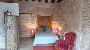 Een slaapkamer met een bed, twee nachtkastjes met lampen, een stoel en een decoratief wandtapijt.