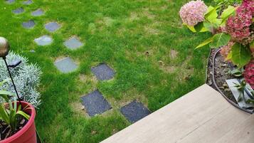 Een verzorgde tuin met gazon, natuurstenen pad, bloembakken en een stenen muur.