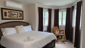 A neatly made bed with white linens and a rolled towel, a wooden chair, and a framed picture on the wall. - LaPlaya House 5 minutes from the best beaches! Ideal house for families (Manati)