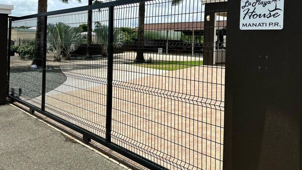 A gated area with palm trees, a sign for 'La Playa House Manati P.R.', and a paved courtyard. - LaPlaya House 5 minutes from the best beaches! Ideal house for families (Manati)