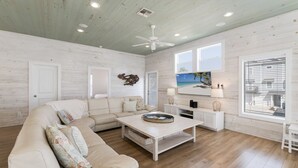 A spacious living room with a beige sofa, a coffee table, and a TV mounted on the wall. - No Agenda Hacienda QUARTER MILE WALK TO BEACH (Port Aransas)