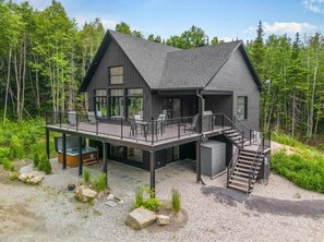 A modern two-story cabin with a deck, outdoor seating, and a hot tub. - Hôtel à la maison - Chalet Yasumi (Petite-Rivière-Saint-François)