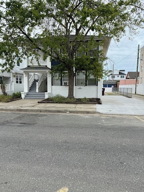 A two-story building with a white exterior, a front porch, and a tree in front. - Spacious 4BR Retreat - Walk to Dining + Beach Gear (Ventnor City)