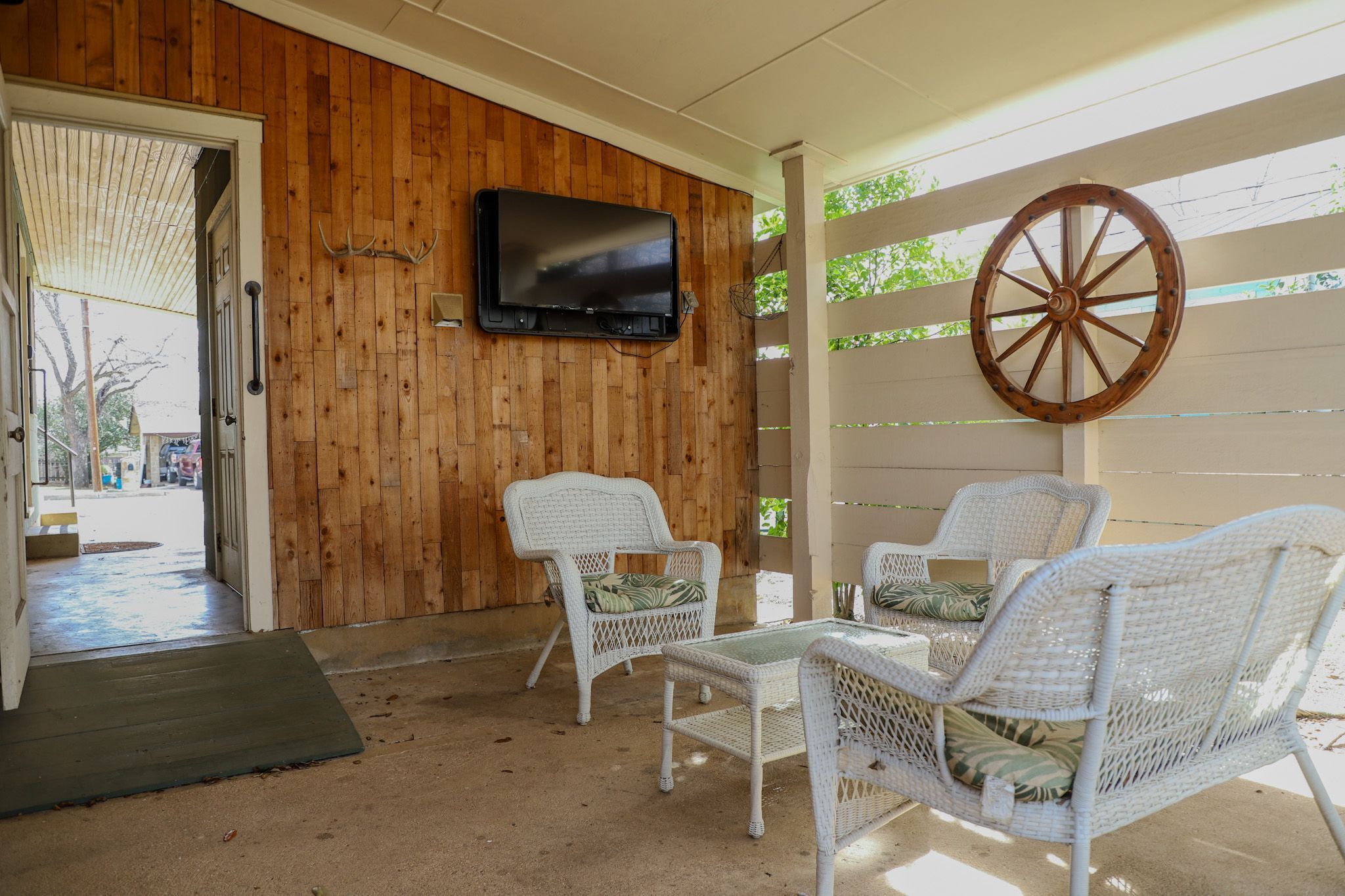 A covered outdoor seating area with wicker furniture and a mounted TV.