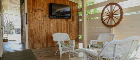 A covered outdoor seating area with wicker furniture and a mounted TV.