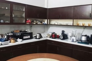 A kitchen with dark wooden cabinets, a microwave, a kettle, a coffee maker, and various kitchen utensils. - DoubleTree House (Chiang Mai)