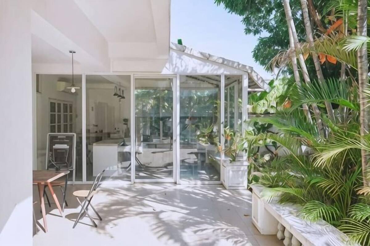 A modern outdoor space with a glass enclosure, a dining area, and lush tropical plants.