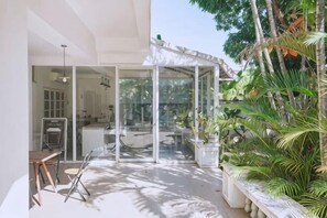 A modern outdoor space with a glass enclosure, a dining area, and lush tropical plants. - DoubleTree House (Chiang Mai)