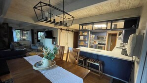 A modern kitchen with a central island, wooden chairs, and a dining table with a white table runner.
