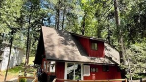 A red cabin with a wooden deck, a staircase, and a covered outdoor seating area.