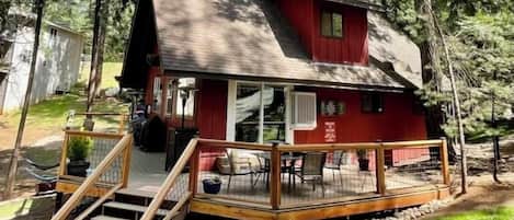 Une cabane rouge avec une terrasse en bois, un escalier et un espace extérieur aménagé et abrité.