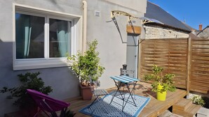 Un patio con mesa y sillas de madera, plantas en macetas y una ventana.