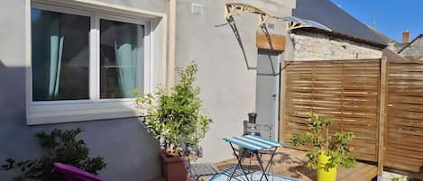 A patio with a wooden table, chairs, potted plants, and a window.
