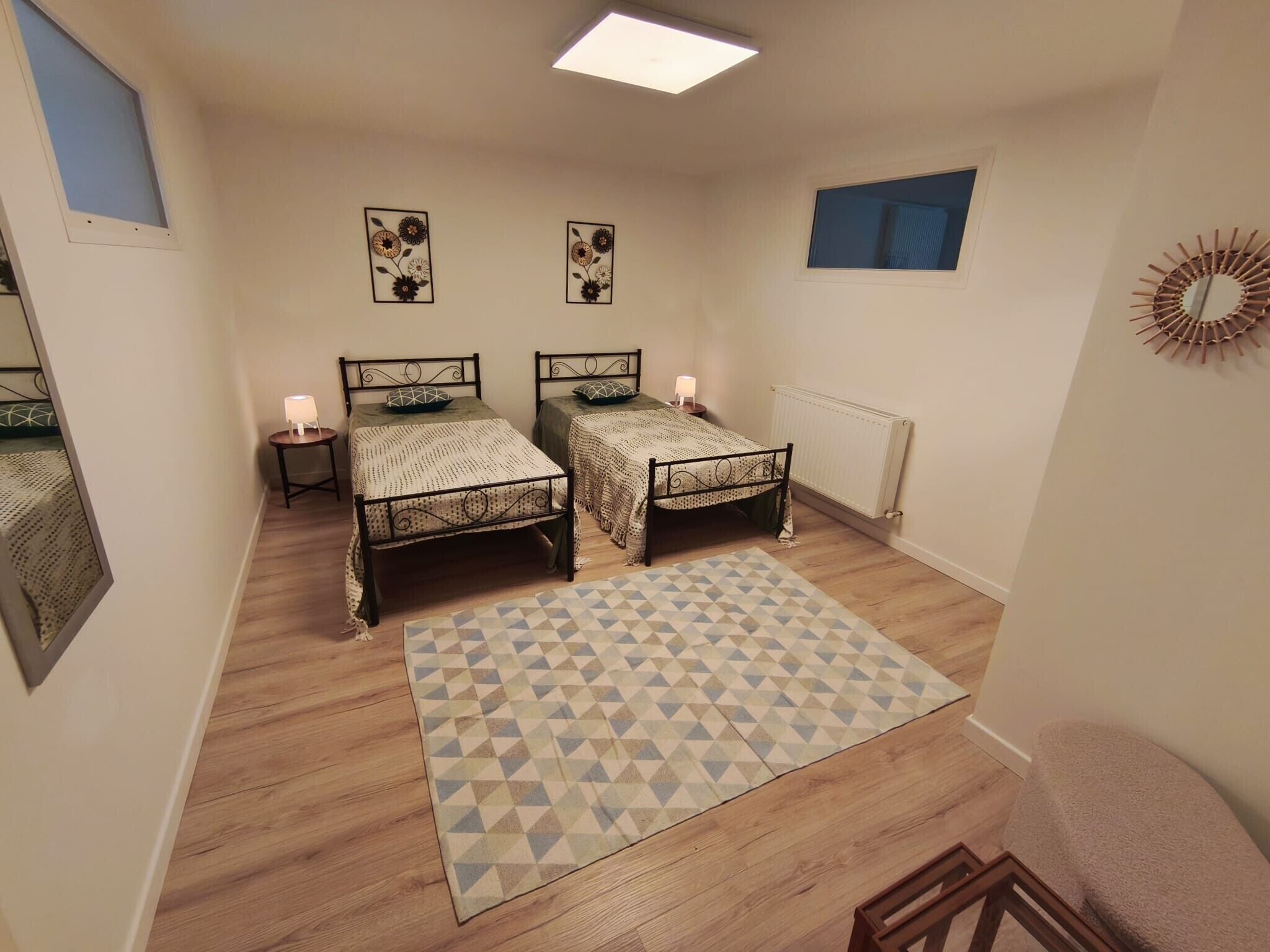 Une chambre avec deux lits, un tapis à motifs, un radiateur et des œuvres d’art murales.