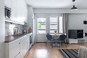 A modern kitchen with white cabinets, a built-in oven, and a microwave. There is a dining area with a table and chairs, and a TV on a stand. - Apartments with Sauna, Balcony & Free Parking (Lahti)