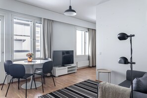 A modern living room with a dining area, a flat-screen TV, and a large window with curtains. - Apartments with Sauna, Balcony & Free Parking (Lahti)