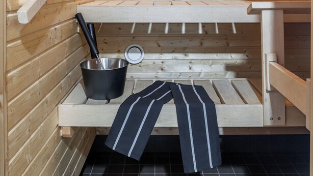Un sauna avec des murs en bois, un banc, une étagère avec un seau et une serviette.