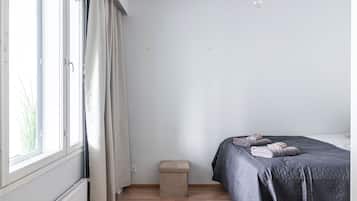Une chambre à coucher avec un lit, un petit tabouret, un radiateur et une fenêtre avec des rideaux.