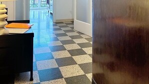 Een hotel lobby met een geruit vloertapijt, een bureau met een lamp en een deur met een sleutelgat.