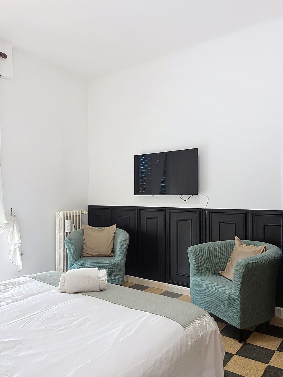 A hotel room with a bed, two armchairs, a television, and a radiator.
