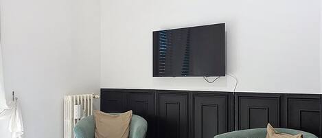 A hotel room with a bed, two armchairs, a television, and a radiator.