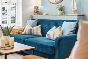 Ein blaues Sofa mit gestreiften Kissen, ein kleiner Tisch mit Kerzen und eine Pflanze.