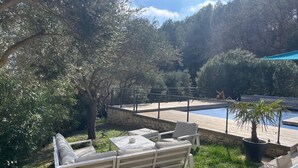 A pool area with a wooden deck, lounge chairs, and a stone wall. - Villa Oriel Naturiste (Figanières)