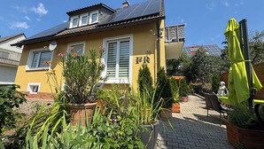 A yellow building with a tiled roof, a bench, and potted plants in the foreground. - Vacation apartment (50sqm) with balcony and sun terrace in Frickenhausen (Frickenhausen)