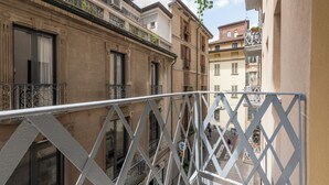 A narrow street with buildings on either side, featuring balconies with metal railings and windows with shutters. - Milan Royal Suites Duomo (Milan)