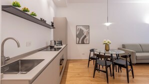 A modern kitchen with a built-in sink, a dining area with a round table and chairs, and a grey sofa in the living area. - Milan Royal Suites Duomo (Milan)