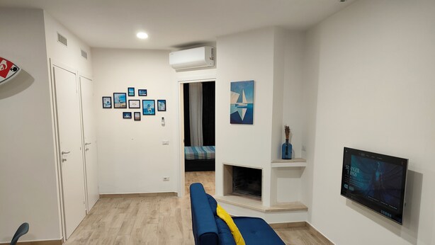 A modern living room with a blue sofa, a fireplace, a mounted TV, and framed pictures on the wall. - Gisella Surf House (Ladispoli)