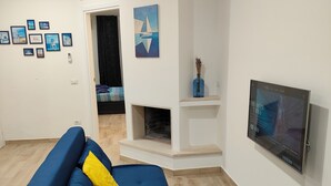 A living room with a blue sofa, a fireplace, a mounted TV, and a wall with framed pictures. - Gisella Surf House (Ladispoli)
