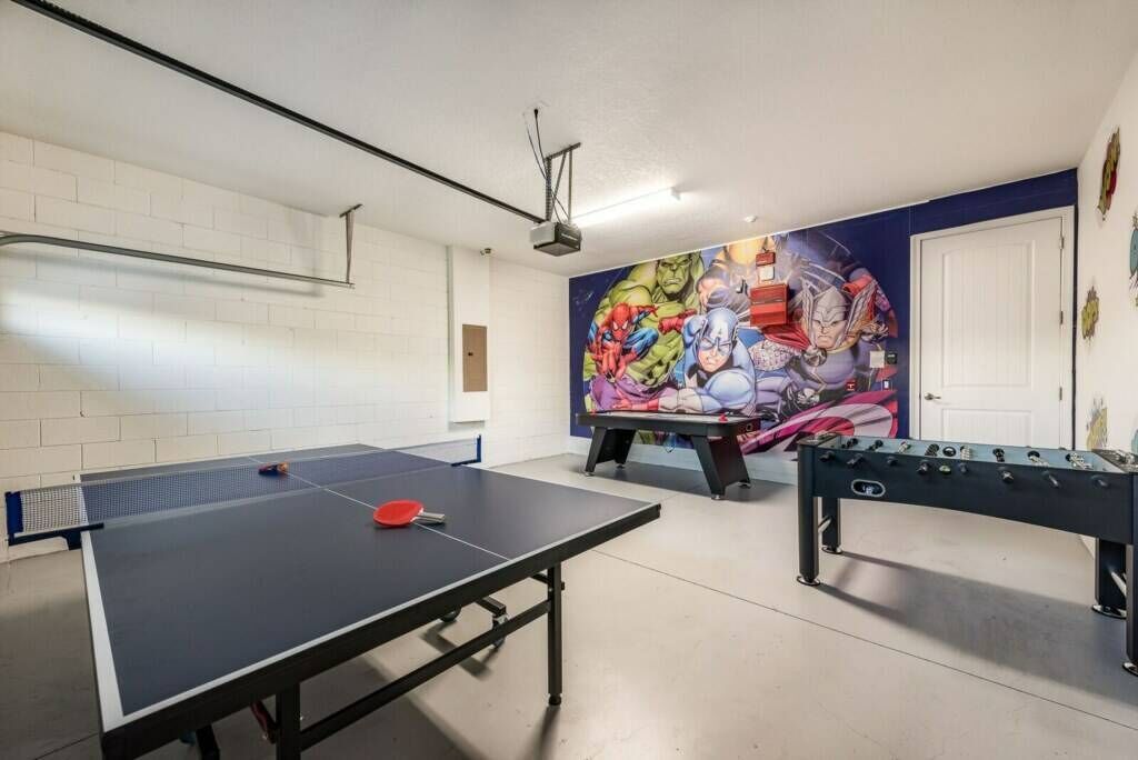 Una stanza con tavolo da ping pong, tavolo da calcio e un murale con supereroi al muro.