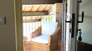 Una silla de mimbre con cojín blanco en un patio al aire libre con suelo de ladrillo y techo de madera.