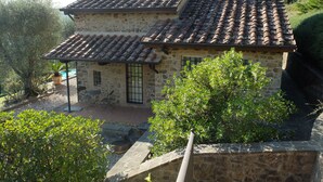 Una casa de piedra con techo de tejas, un pequeño patio y una piscina.