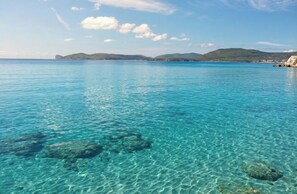 A clear blue sea with visible underwater rocks and a distant coastline with hills. - ClickSardegna Rafel Penthouse Facing San Giovanni Beach, with Terrace (Alghero)