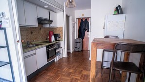 A compact kitchen with a wooden herringbone floor, a dining area with a wooden table and metal chairs, and a white refrigerator. - Modern accommodation, near Parisian attractions (Paris)