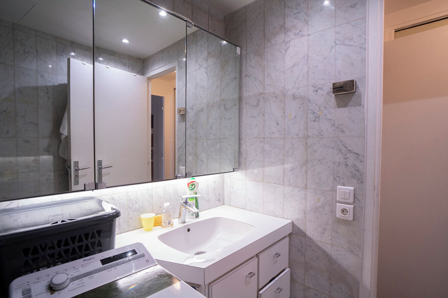 A modern bathroom with a marble wall, a large mirror, a white sink, and a handheld radio.