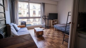 A compact hotel room with a sofa, a bed, a TV, and a window with a view of a building. - Modern accommodation, near Parisian attractions (Paris)